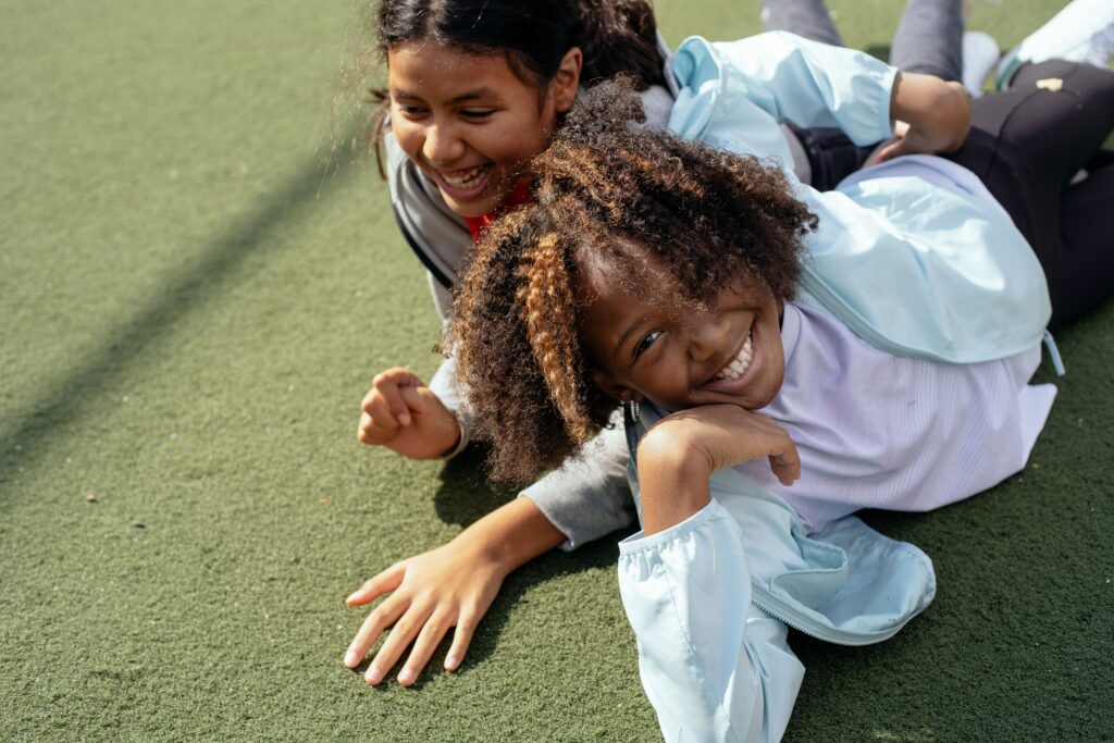 Cheerful multiracial girls lying on sports ground and smiling while spending sunny day together
