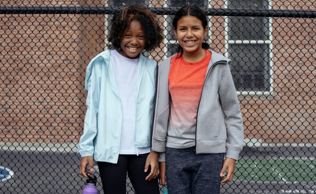 Cheerful multiracial athletes in sportswear standing together near metal net fence and looking at camera
